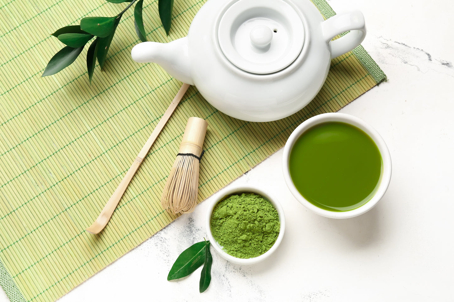 A flat-lay image of vibrant green matcha powder with a whisk, spoon, and teacup on a green placemat